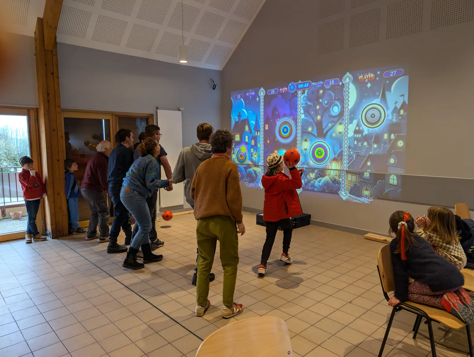 Familles jouant ensemble au ballon sur le mur interactif Kmoove en salle polyvalente
